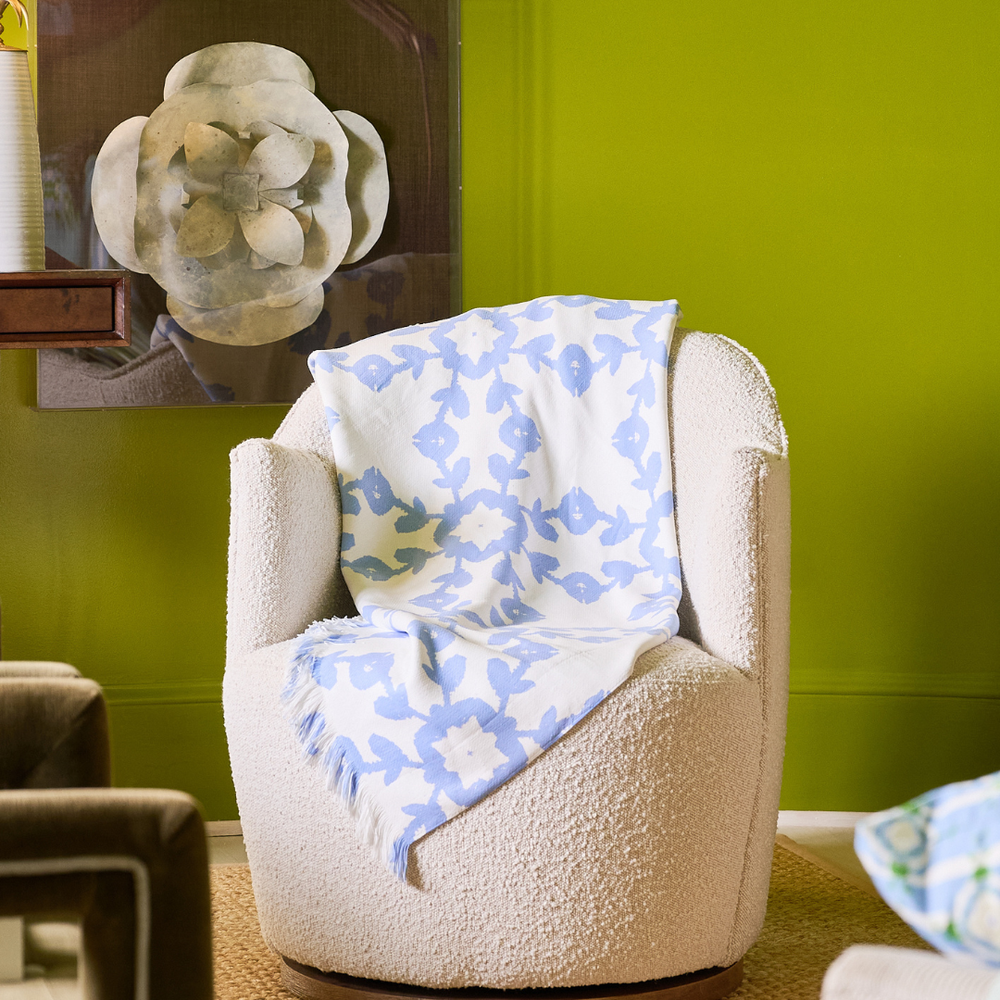 Beige armchair with a blue and white patterned blanket against a green wall.