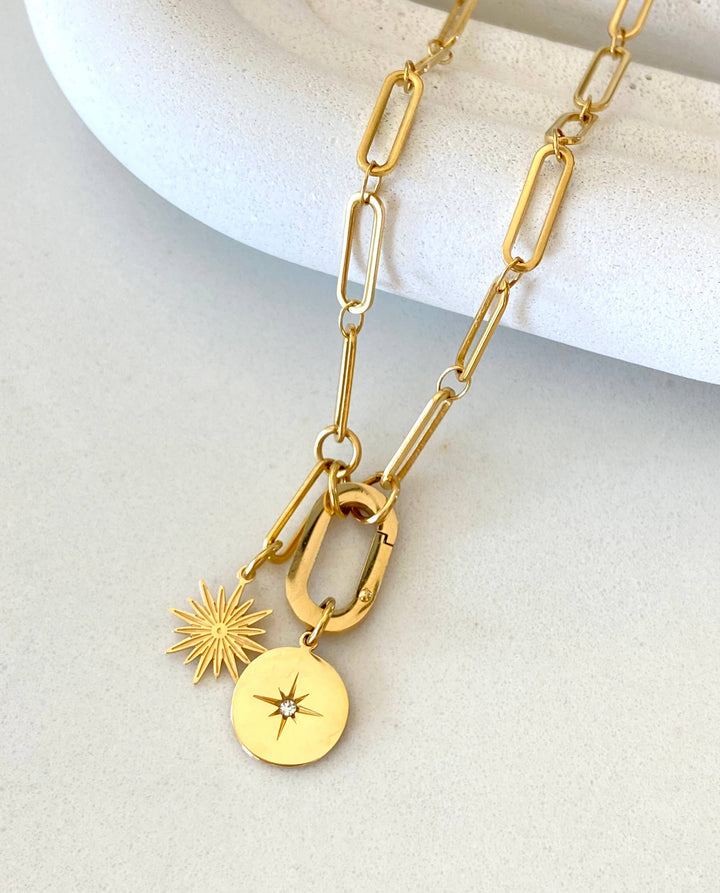 Gold necklace with star and disc pendants on a light background