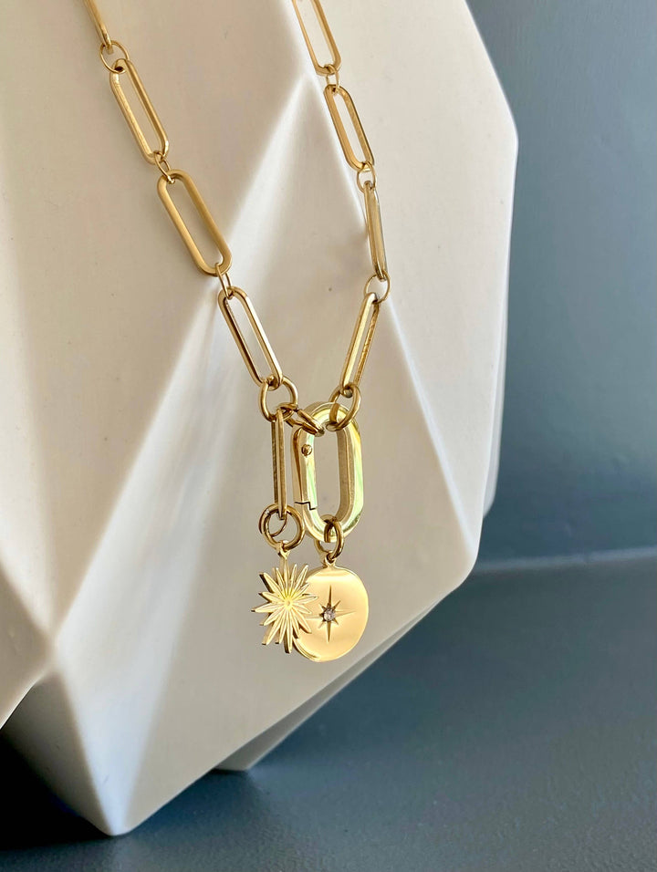 Gold necklace with charms on a white geometric object against a blue background