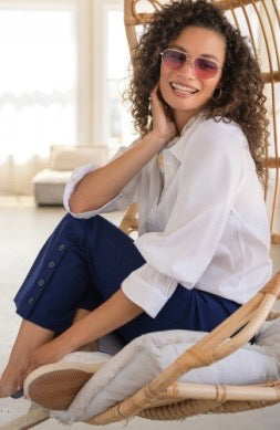 Woman sitting on a wicker chair wearing sunglasses and a white shirt with a blurred background