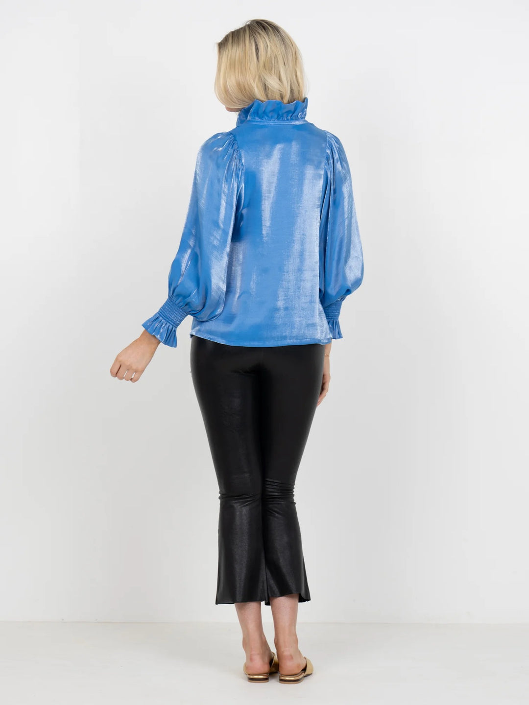Person wearing a blue shiny top and black pants on a white background
