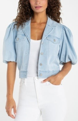 Woman wearing a light blue denim jacket over a white top and pants on a white background