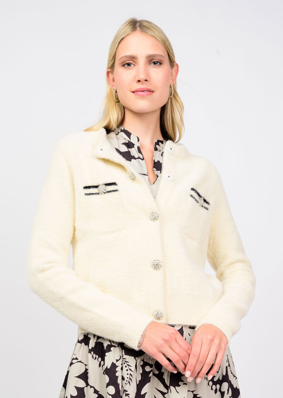 Woman wearing a cream-colored cardigan with black accents on a white background