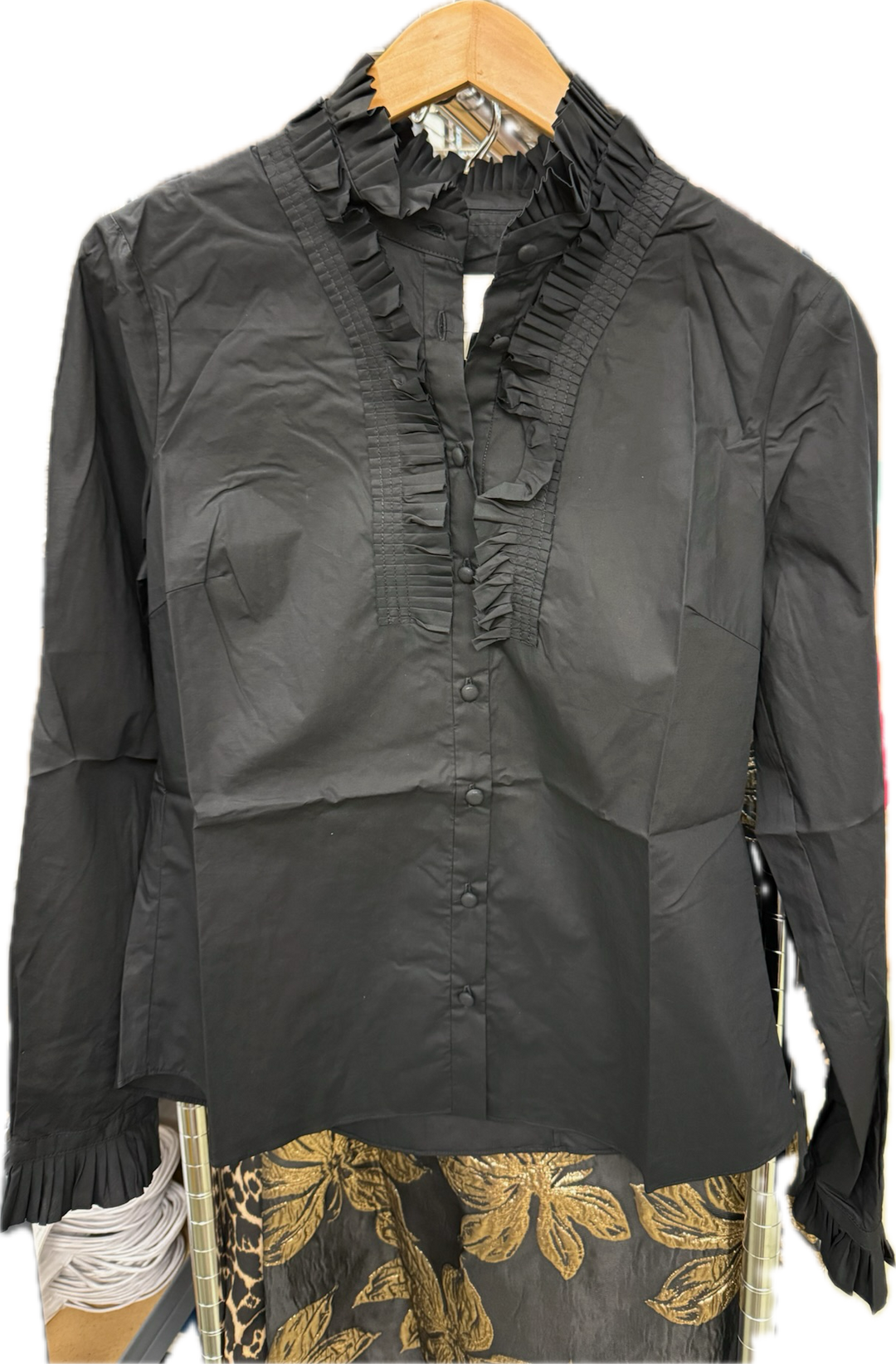 Black blouse with ruffled details on a hanger against a white background