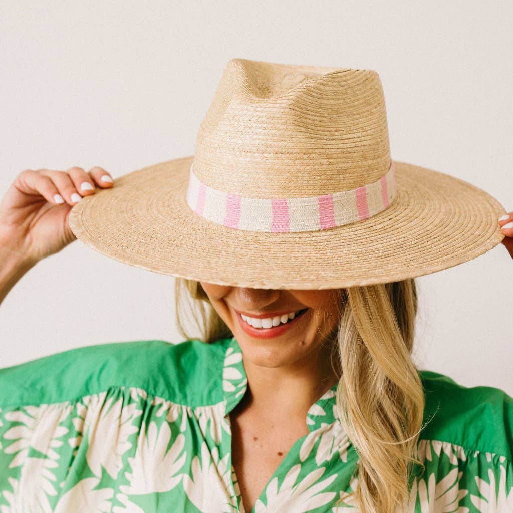 Woman wearing a straw hat with a pink band against a plain background