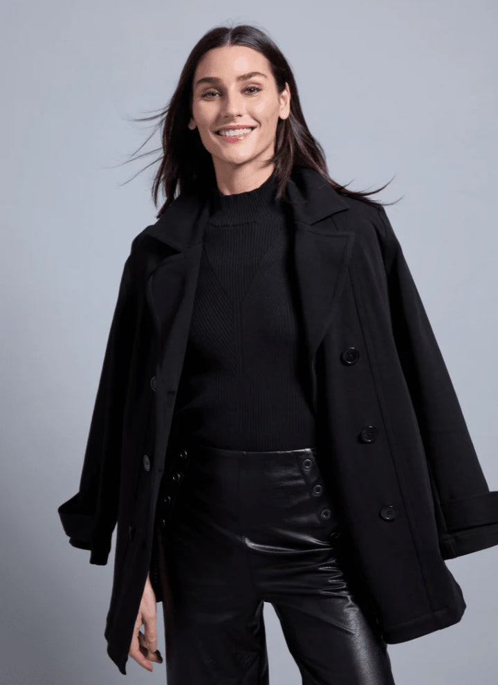 Woman wearing a black coat over a black top and leather pants on a gray background