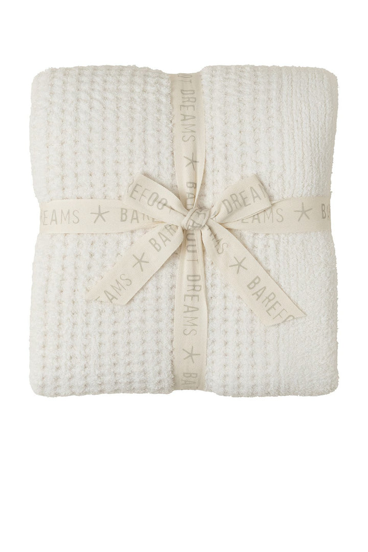 Soft beige barefoot dreams Cozy Waffle Throw draped on a sofa, showcasing its textured waffle pattern and plush fabric.
