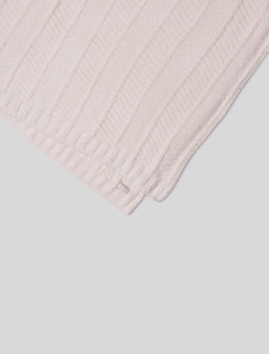 Barefoot Dreams cozy herringbone bed blanket draped over a bed, featuring soft, textured fabric in a warm, neutral tone.
