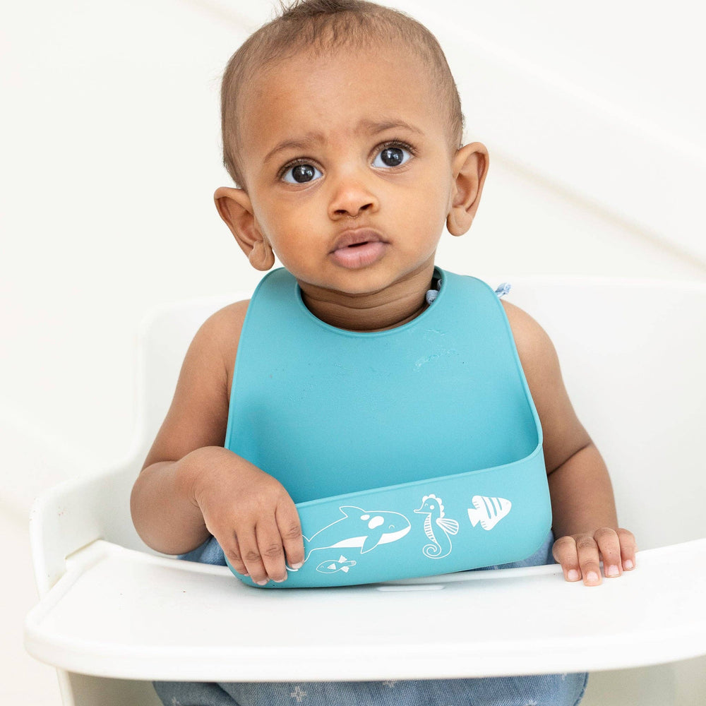Baby wearing Ocean Friends Starter Bib by Bella Tunno with colorful ocean animal illustrations.