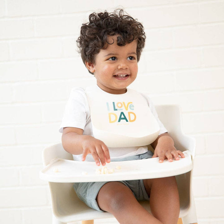 Baby wearing Bella Tunno I Love Dad Wonder Bib, colorful silicone bib with adjustable neck strap for easy feeding cleanup.