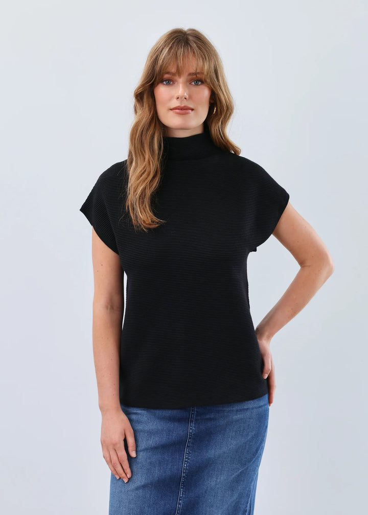 Woman wearing a black turtleneck top and blue jeans against a light gray background