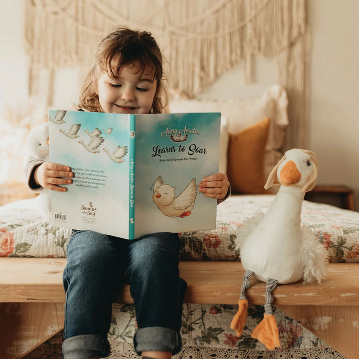 Baby wearing Avery the Aviator plush book by Bunnies by the Bay, featuring soft fabric and colorful illustrations for little ones.