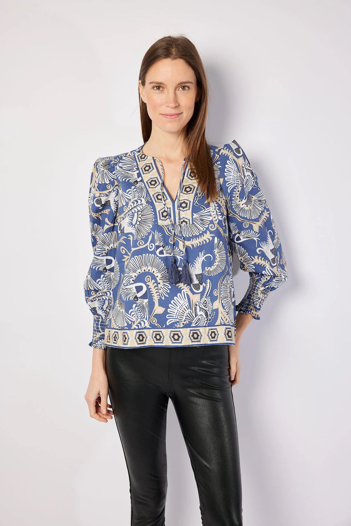Woman wearing a blue patterned blouse with black pants on a white background