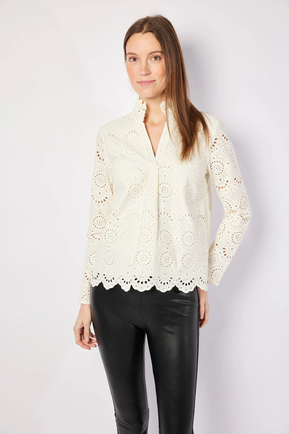Woman wearing a white lace blouse and black pants on a plain background