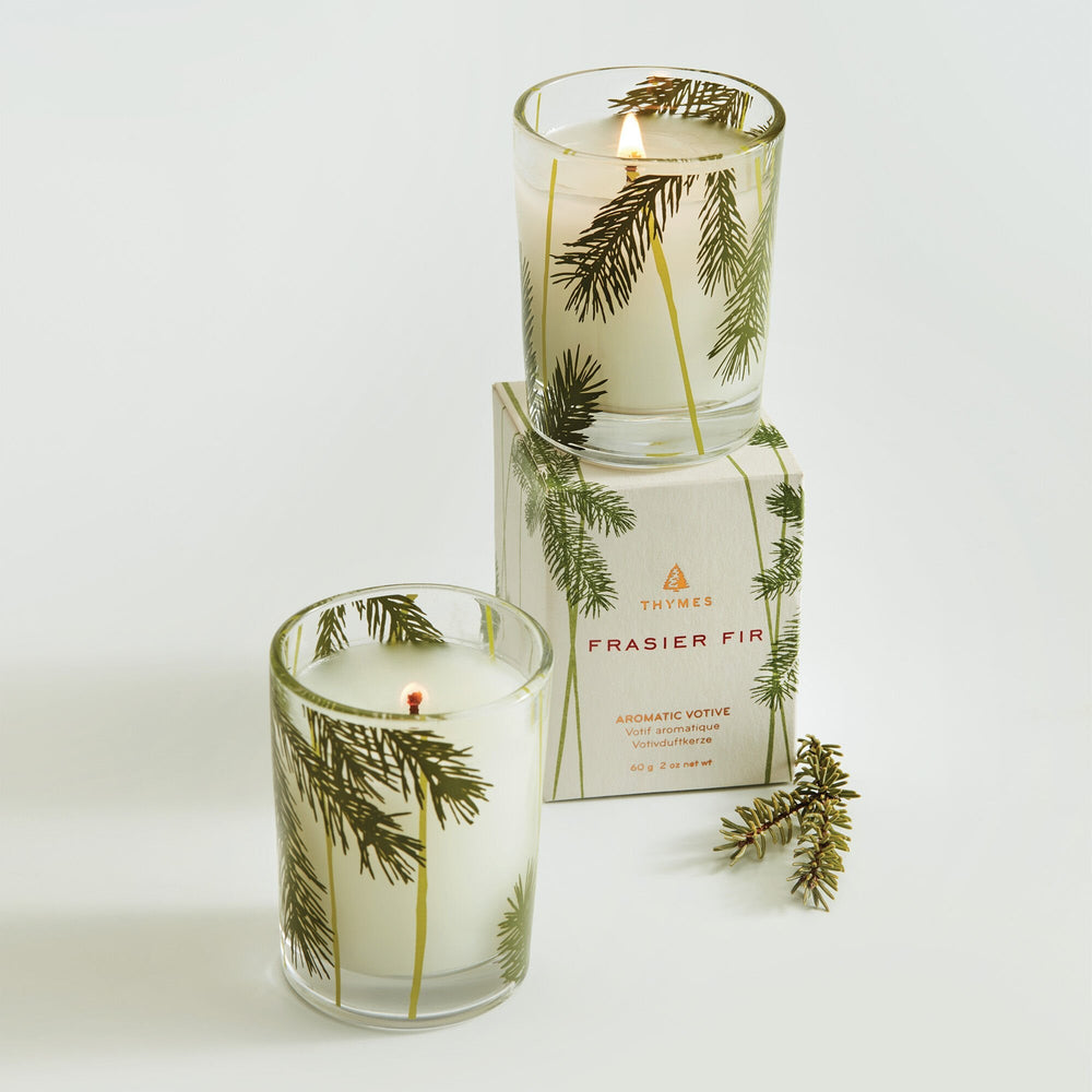 Thymes Frasier Fir Pine Needle Votive Candle with a tall glass holder, showcasing a festive scent and natural pine needle design.