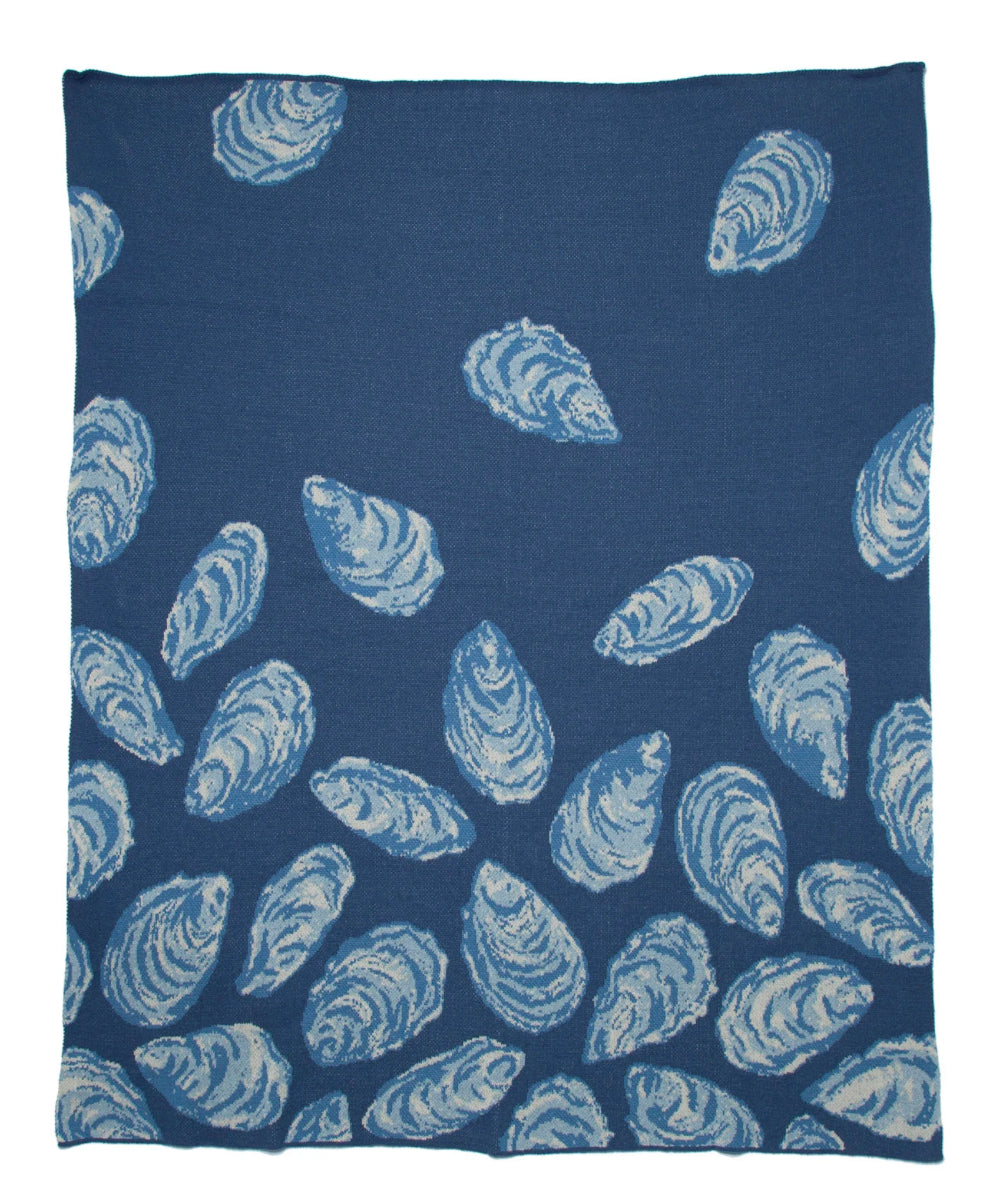 In2Green oyster throw blanket made from recycled cotton, cozy and eco-friendly home decor accessory displayed on a sofa.