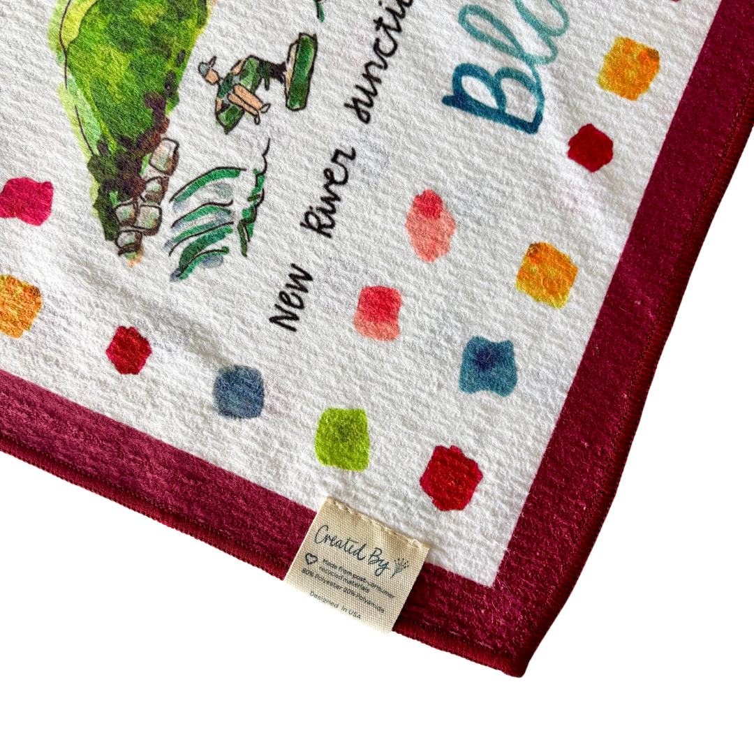 Keva Style Blacksburg tea towel with a decorative pattern, displayed hanging on a wooden rod in a home kitchen setting.