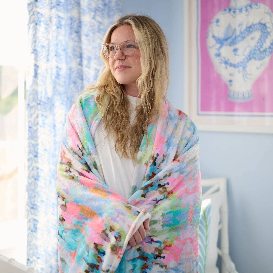Laura Park Designs Brooks Avenue Fleece Blanket shown spread out on a cozy home setting, featuring soft, plush fabric in neutral tones.