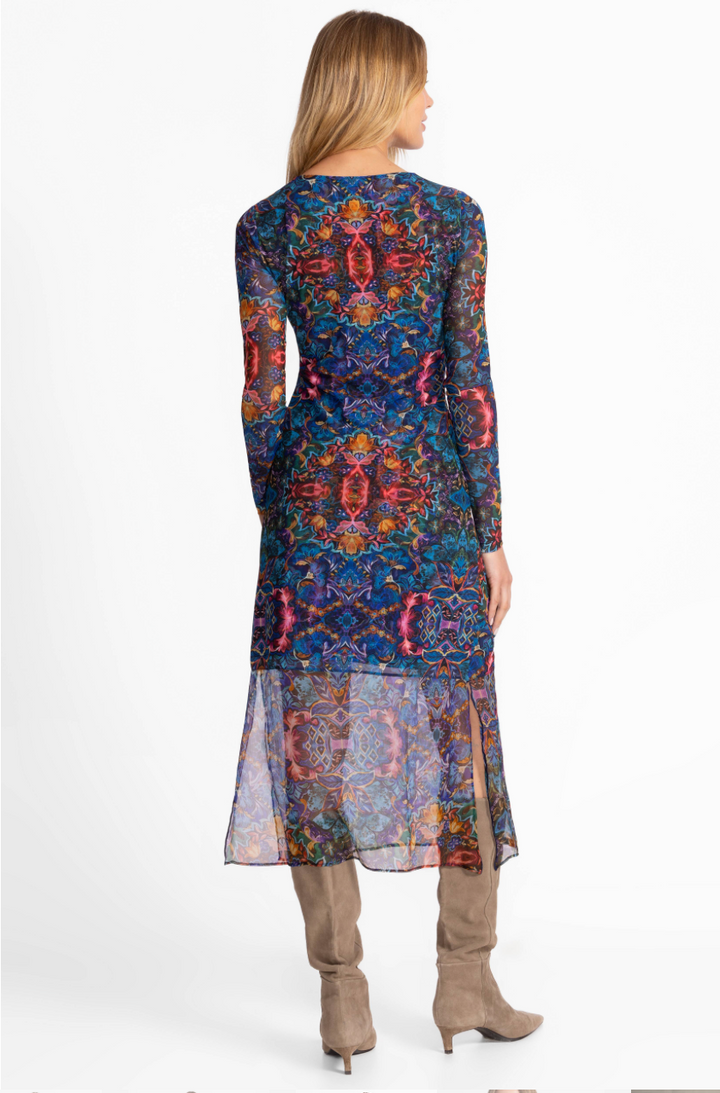 Woman wearing a long, patterned dress with sheer overlay on a white background