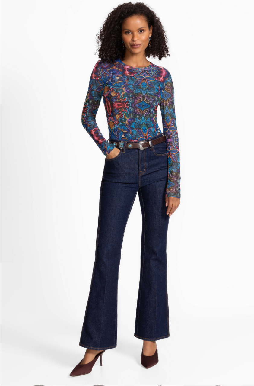 Woman wearing a patterned top and dark blue jeans on a white background