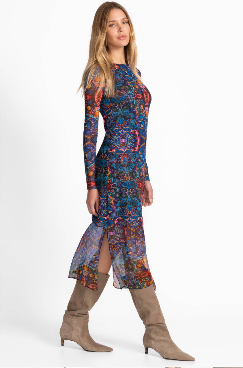 Woman wearing a colorful patterned dress with long sleeves and a slit, standing against a white background.
