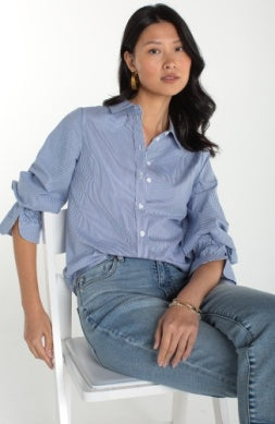Woman wearing a blue shirt and jeans sitting on a white chair against a white background