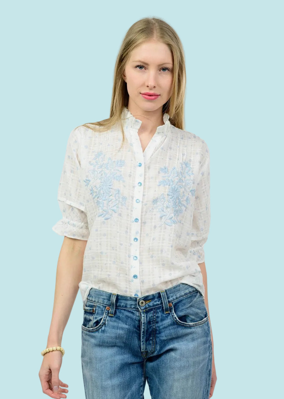 Woman wearing a white blouse with floral patterns and blue jeans on a white background