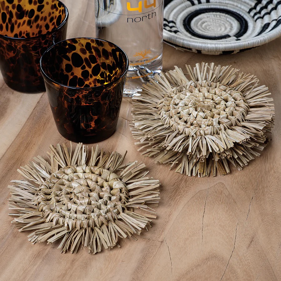 Set of four Zodax fringed coasters with textured fabric and tassel details, perfect for protecting surfaces in home decor.
